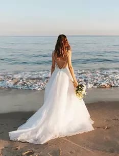 Bride in a flowing gown at the shoreline.
