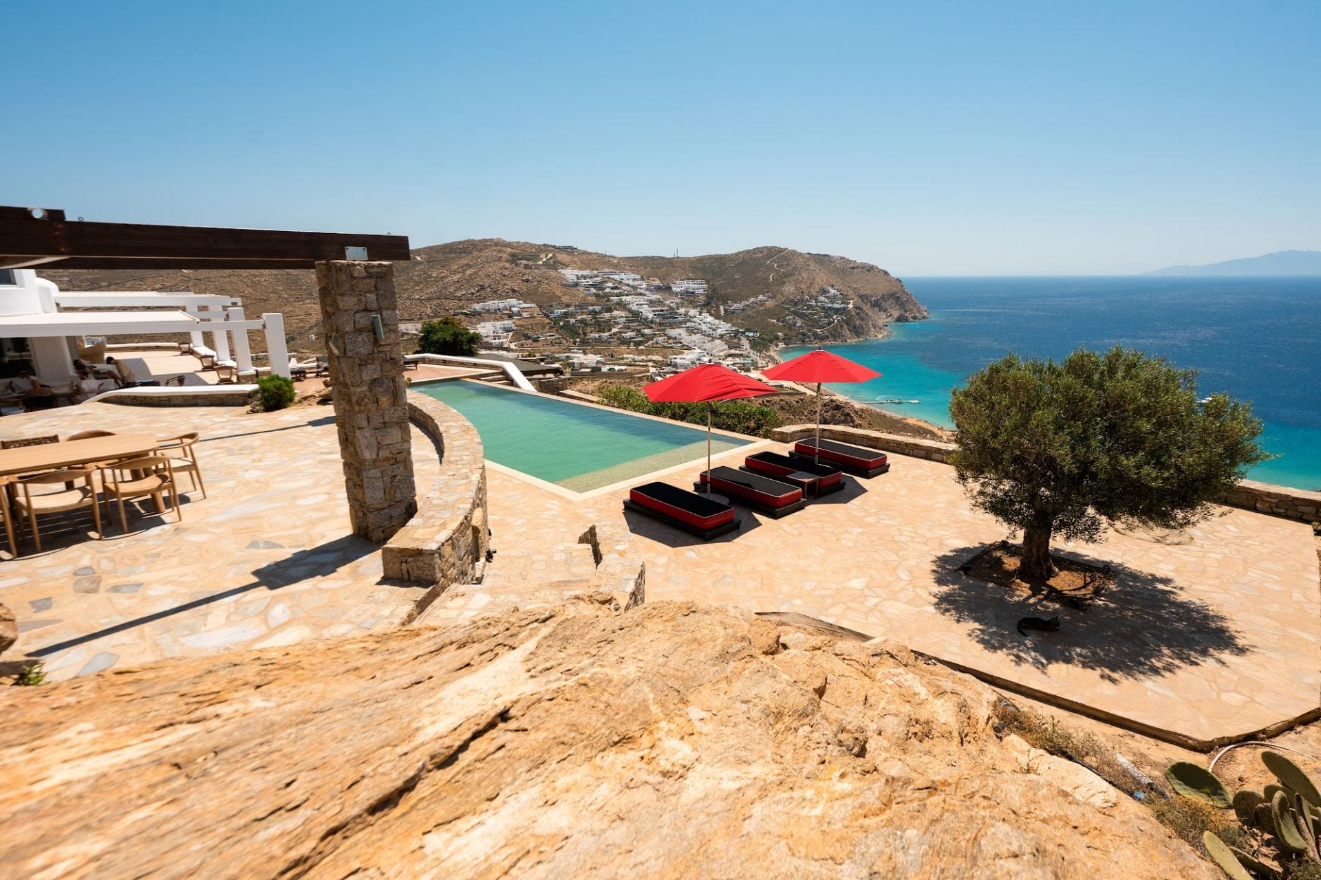 Infinity pool on the cliff with red umbrellas and the Aegean beyond